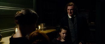 Movie still from “The Man Who Invented Christmas” (2017), directed by Bharat Nalluri – A woman and a child are standing in a dark room; Medium shot, Over the shoulder angle