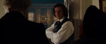 Movie still from “The Man Who Invented Christmas” (2017), directed by Bharat Nalluri – A man in a white shirt and a black tie standing in front of a wall; Medium shot, Over the shoulder angle