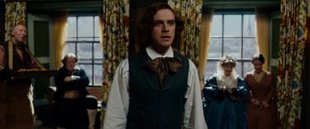 Movie still from “The Man Who Invented Christmas” (2017), directed by Bharat Nalluri – A man in a vest and bow tie standing in front of a window; Medium shot, Over the shoulder angle