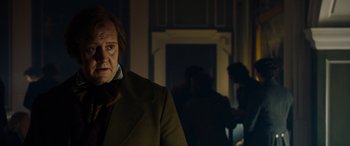 Movie still from “The Man Who Invented Christmas” (2017), directed by Bharat Nalluri – A man standing in a dark room wearing a suit; Medium shot, Over the shoulder angle