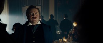 Movie still from “The Man Who Invented Christmas” (2017), directed by Bharat Nalluri – A man standing in front of a group of people in a dark room; Close Up shot, Over the shoulder angle