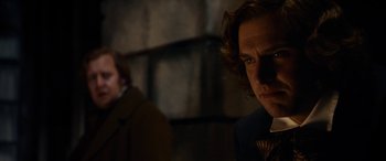 Movie still from “The Man Who Invented Christmas” (2017), directed by Bharat Nalluri – A man in a suit and tie standing next to another man in a suit and tie; Close Up shot, Over the shoulder angle