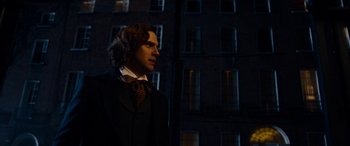 Movie still from “The Man Who Invented Christmas” (2017), directed by Bharat Nalluri – A man standing in front of a building at night; Medium shot, Over the shoulder angle