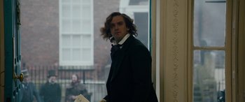 Movie still from “The Man Who Invented Christmas” (2017), directed by Bharat Nalluri – A man with long hair standing in front of a window; Medium shot, Over the shoulder angle