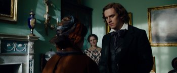 Movie still from “The Man Who Invented Christmas” (2017), directed by Bharat Nalluri – Two women and a man standing in front of a mirror; Medium shot, Over the shoulder angle