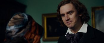 Movie still from “The Man Who Invented Christmas” (2017), directed by Bharat Nalluri – A man with long brown hair wearing a bow tie; Close Up shot, Over the shoulder angle