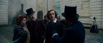 Movie still from “The Man Who Invented Christmas” (2017), directed by Bharat Nalluri – A group of men standing next to each other on a street; Medium shot, Over the shoulder angle