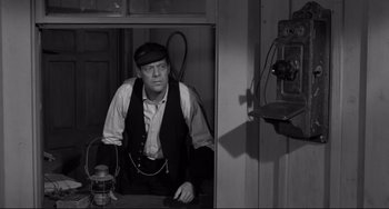 Movie still from “The Man Who Shot Liberty Valance” (1962), directed by John Ford – A man in a black hat and a white shirt is sitting in a room; Medium shot, Over the shoulder angle