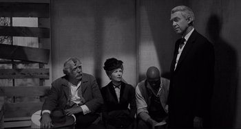 Movie still from “The Man Who Shot Liberty Valance” (1962), directed by John Ford – A group of people sitting next to each other on a bench; Medium shot, Over the shoulder angle