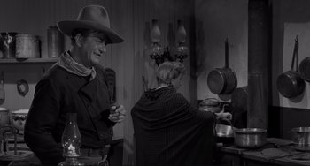 Movie still from “The Man Who Shot Liberty Valance” (1962), directed by John Ford – A black and white photo of a man and a woman in a kitchen; Medium shot, Over the shoulder angle