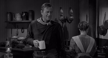 Movie still from “The Man Who Shot Liberty Valance” (1962), directed by John Ford – A man holding a cup in a kitchen; Medium shot, Over the shoulder angle