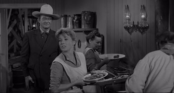 Movie still from “The Man Who Shot Liberty Valance” (1962), directed by John Ford – A group of people standing in a kitchen holding plates; Medium shot, Over the shoulder angle