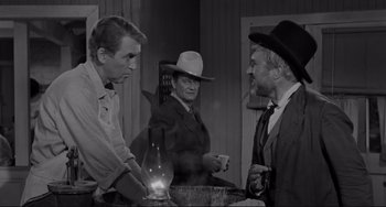 Movie still from “The Man Who Shot Liberty Valance” (1962), directed by John Ford – A man in a suit and a cowboy hat talking to two other men; Medium shot, Over the shoulder angle