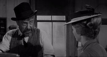 Movie still from “The Man Who Shot Liberty Valance” (1962), directed by John Ford – A man and a woman wearing hats talking to each other in front of a window; Medium shot, Over the shoulder angle