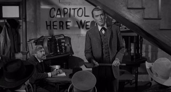 Movie still from “The Man Who Shot Liberty Valance” (1962), directed by John Ford – A black and white photo of a man holding a cane; Medium shot, Over the shoulder angle