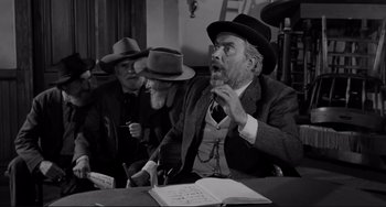 Movie still from “The Man Who Shot Liberty Valance” (1962), directed by John Ford – A man with a surprised look on his face while sitting at a table with two other men; Medium shot, Over the shoulder angle