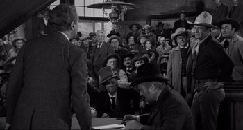 Movie still from “The Man Who Shot Liberty Valance” (1962), directed by John Ford – A crowd of people sitting and standing in a room; Wide shot, Over the shoulder angle