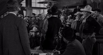 Movie still from “The Man Who Shot Liberty Valance” (1962), directed by John Ford – A group of people in a room with hats on; Wide shot, Over the shoulder angle