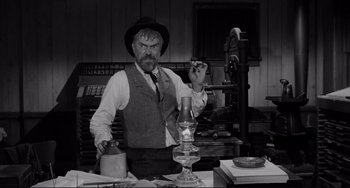 Movie still from “The Man Who Shot Liberty Valance” (1962), directed by John Ford – An old man sitting at a desk with a pipe in his mouth; Medium shot, Low angle