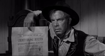 Movie still from “The Man Who Shot Liberty Valance” (1962), directed by John Ford – A man holding a newspaper while wearing a cowboy hat; Close Up shot, Low angle