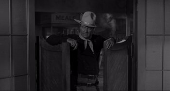 Movie still from “The Man Who Shot Liberty Valance” (1962), directed by John Ford – A man wearing a cowboy hat standing next to a wooden fence; Medium shot, Over the shoulder angle