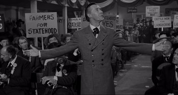 Movie still from “The Man Who Shot Liberty Valance” (1962), directed by John Ford – A man wearing a suit and tie in front of a crowd of people; Medium shot, Low angle