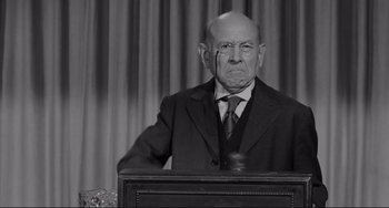 Movie still from “The Man Who Shot Liberty Valance” (1962), directed by John Ford – An old man in a suit and tie standing in front of a microphone; Medium shot, Low angle