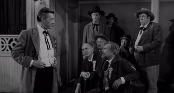 Movie still from “The Man Who Shot Liberty Valance” (1962), directed by John Ford – A black and white photo of a group of men in suits and hats; Medium shot, Over the shoulder angle