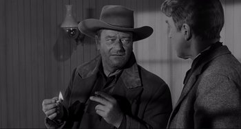 Movie still from “The Man Who Shot Liberty Valance” (1962), directed by John Ford – A black and white photo of a man in a hat; Medium shot, Over the shoulder angle