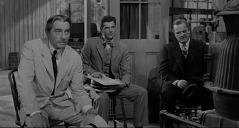 Movie still from “The Man Who Shot Liberty Valance” (1962), directed by John Ford – A group of men sitting on stools next to each other; Medium shot, Over the shoulder angle