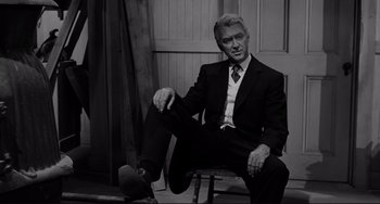 Movie still from “The Man Who Shot Liberty Valance” (1962), directed by John Ford – Black and white photograph of a man sitting on a stool; Medium shot, Low angle
