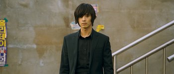 A man in a black suit standing in front of a wall