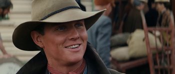 Movie still from “The Man from Snowy River” (1982), directed by George Miller – A person wearing a hat and smiling; Close Up shot, Over the shoulder angle
