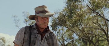 Movie still from “The Man from Snowy River” (1982), directed by George Miller – An older man wearing a cowboy hat and a plaid shirt; Close Up shot, Low angle