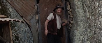 Movie still from “The Man from Snowy River” (1982), directed by George Miller – An old man standing in a doorway holding a pair of scissors; Medium shot, Low angle