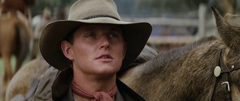 Movie still from “The Man from Snowy River” (1982), directed by George Miller – A man wearing a cowboy hat while standing next to a horse; Close Up shot, Low angle