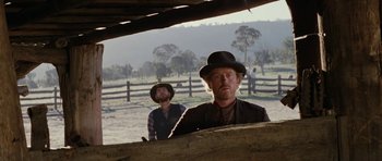Movie still from “The Man from Snowy River” (1982), directed by George Miller – Two men are standing in front of a wooden fence; Medium shot, Low angle