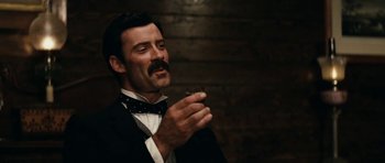 Movie still from “The Man from Snowy River” (1982), directed by George Miller – A man in a suit and bow tie holding a piece of cake; Close Up shot, Low angle