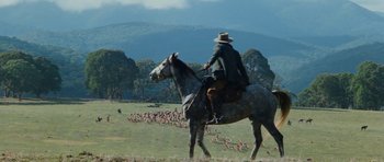 Movie still from “The Man from Snowy River” (1982), directed by George Miller – A man riding a horse in a field with a herd of birds in the background; Wide shot, Low angle