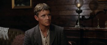 Movie still from “The Man from Snowy River” (1982), directed by George Miller – A man sitting in a chair wearing a suit; Close Up shot, Over the shoulder angle