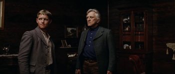 Movie still from “The Man from Snowy River” (1982), directed by George Miller – An older man standing in front of a wooden wall; Medium shot, Low angle
