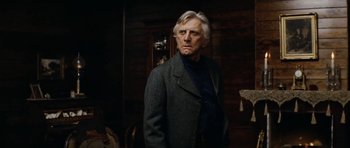 Movie still from “The Man from Snowy River” (1982), directed by George Miller – An older man wearing a jacket and a sweater; Medium shot, Low angle