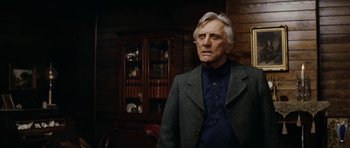 Movie still from “The Man from Snowy River” (1982), directed by George Miller – An older man standing in front of a wooden cabinet; Close Up shot, Low angle