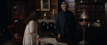 Movie still from “The Man from Snowy River” (1982), directed by George Miller – A man and a woman standing at a wooden table; Medium shot, Low angle