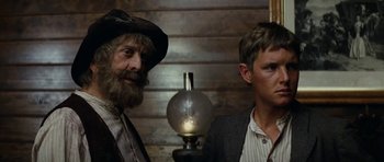 Movie still from “The Man from Snowy River” (1982), directed by George Miller – A man and a boy standing next to each other in front of an oil lamp; Close Up shot, Low angle