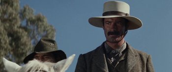 Movie still from “The Man from Snowy River” (1982), directed by George Miller – A man with a hat and a mustache standing next to a dog; Close Up shot, Low angle