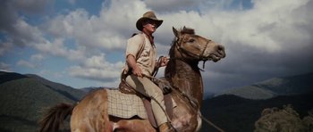 Movie still from “The Man from Snowy River” (1982), directed by George Miller – A man riding on the back of a brown horse; Medium shot, Low angle