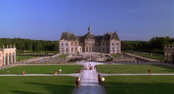 Movie still from “The Man in the Iron Mask” (1998), directed by Randall Wallace – People are sitting in the grass in front of a large building; Extreme Wide shot, High angle