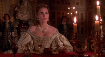 Movie still from “The Man in the Iron Mask” (1998), directed by Randall Wallace – A woman sitting at a dinner table with a glass of wine; Medium shot, Over the shoulder angle
