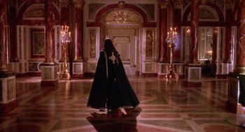 Movie still from “The Man in the Iron Mask” (1998), directed by Randall Wallace – A woman in a black cape walking in a room; Extreme Wide shot, High angle